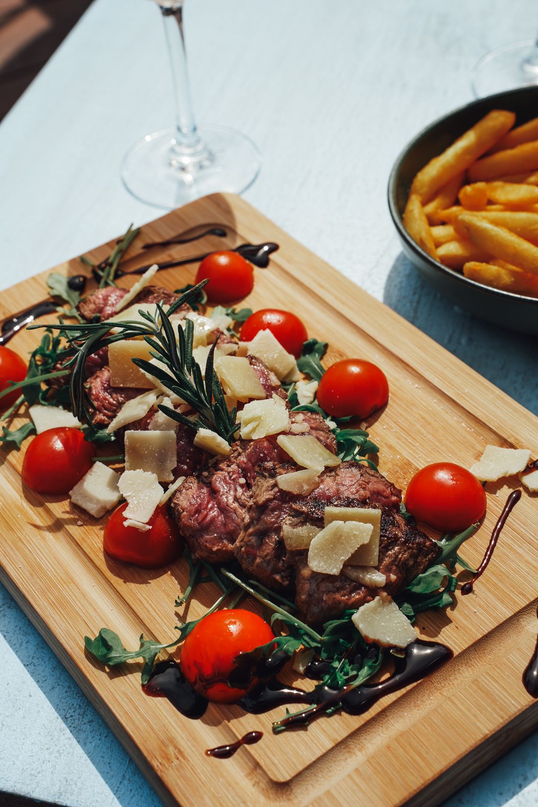 Une tagliata de bœuf sur planche en bois, tomates cerises, roquette et copeaux de parmesan